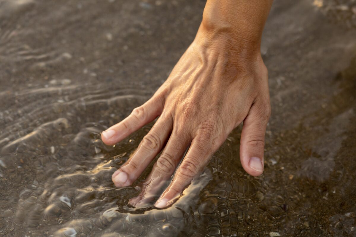 persona-poniendo-su-mano-en-el-agua-en-la-playa